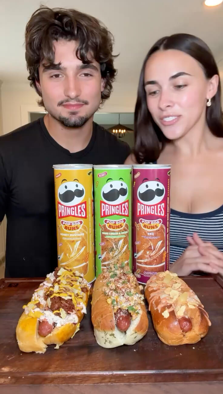 Video thumbnail, Celina and Cenzo stand behind three Pringles Pop Dog Buns cans and three loaded hot dogs.